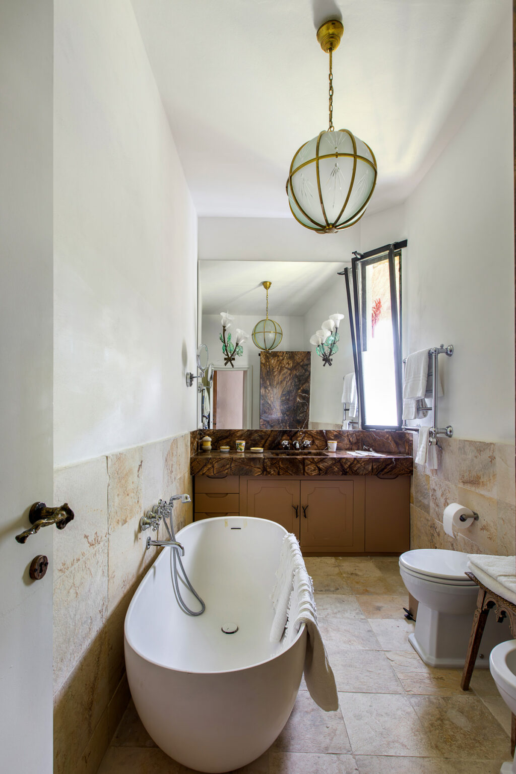 Modern bathroom interior featuring a stylish bathtub, marble countertop, decorative wall art, and natural light from a window. The design combines functionality with aesthetic appeal, ideal for contemporary home decor. | Only on SopranoVillas