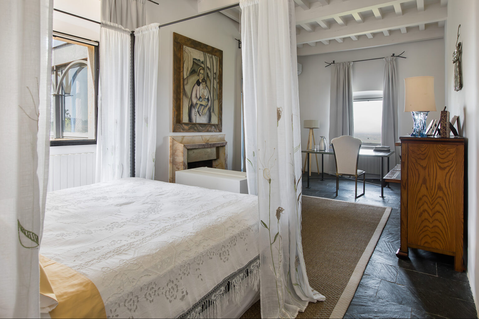 Bright and airy bedroom featuring a cozy bed with decorative linens, a stylish armchair, a wooden dresser, and an elegant workspace. Soft natural light filters through sheer curtains, enhancing the serene atmosphere. | Only on SopranoVillas