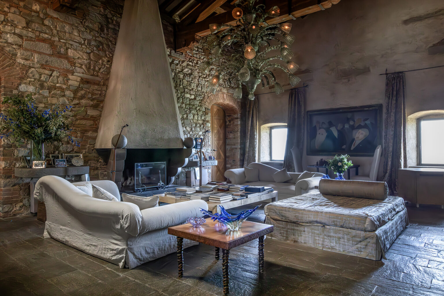 Cozy living room featuring a stone wall, a modern fireplace, plush sofas, and a wooden coffee table adorned with flowers, creating a warm and inviting atmosphere. | Only on SopranoVillas