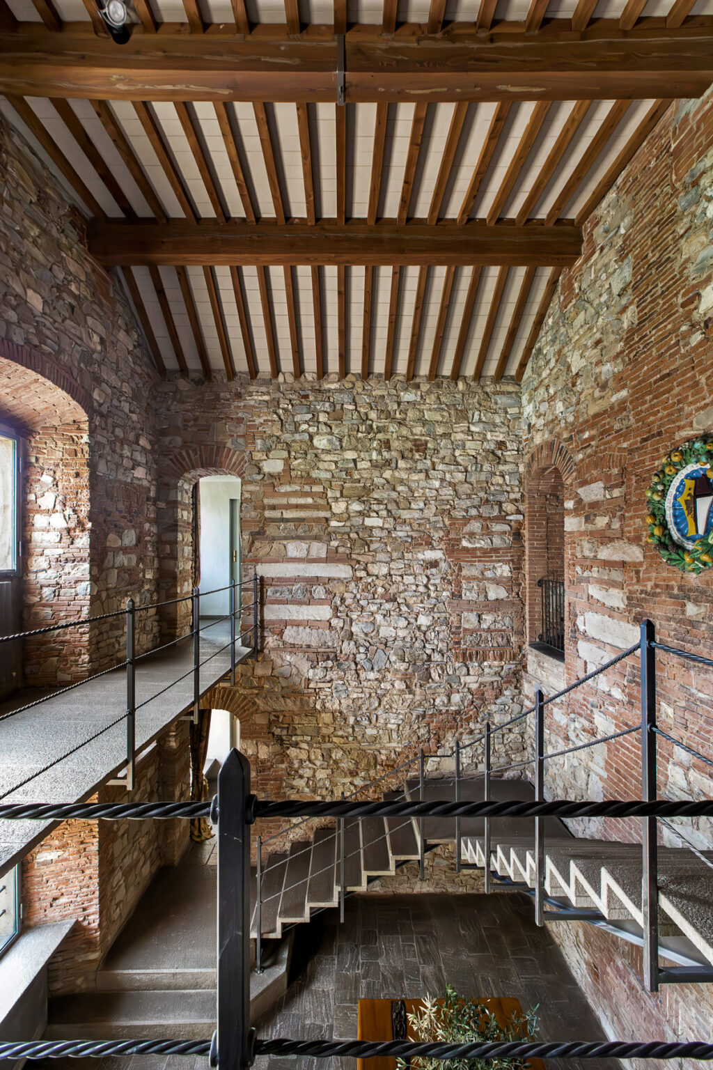Interior view of a historic stone tower featuring exposed brick walls, wooden beams, and a metal walkway, showcasing architectural details and a decorative emblem on the wall. | Only on SopranoVillas