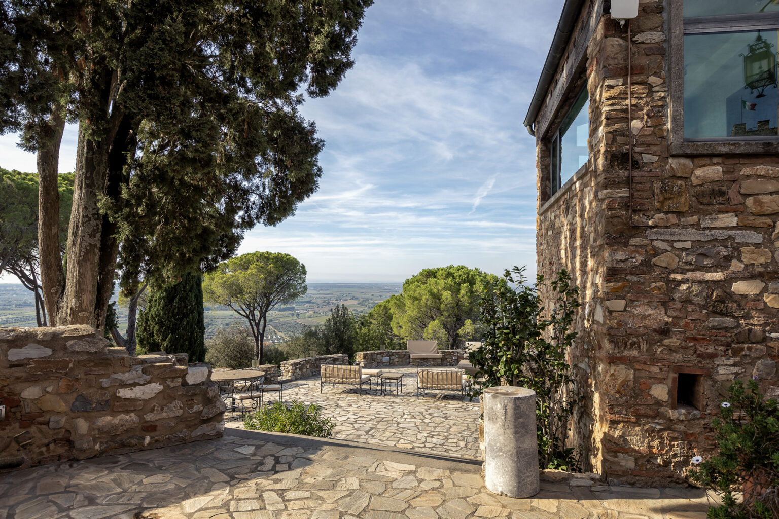 Scenic view of a stone pathway leading to a landscape with trees and rolling hills, framed by a rustic stone building and clear blue sky. | Only on SopranoVillas