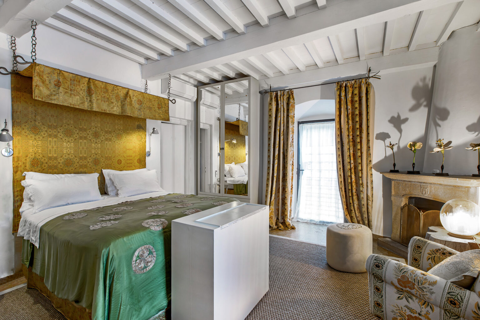 Luxurious hotel room featuring a stylish bed with a green throw, elegant curtains, and a cozy fireplace, designed for comfort and relaxation. | Only on SopranoVillas