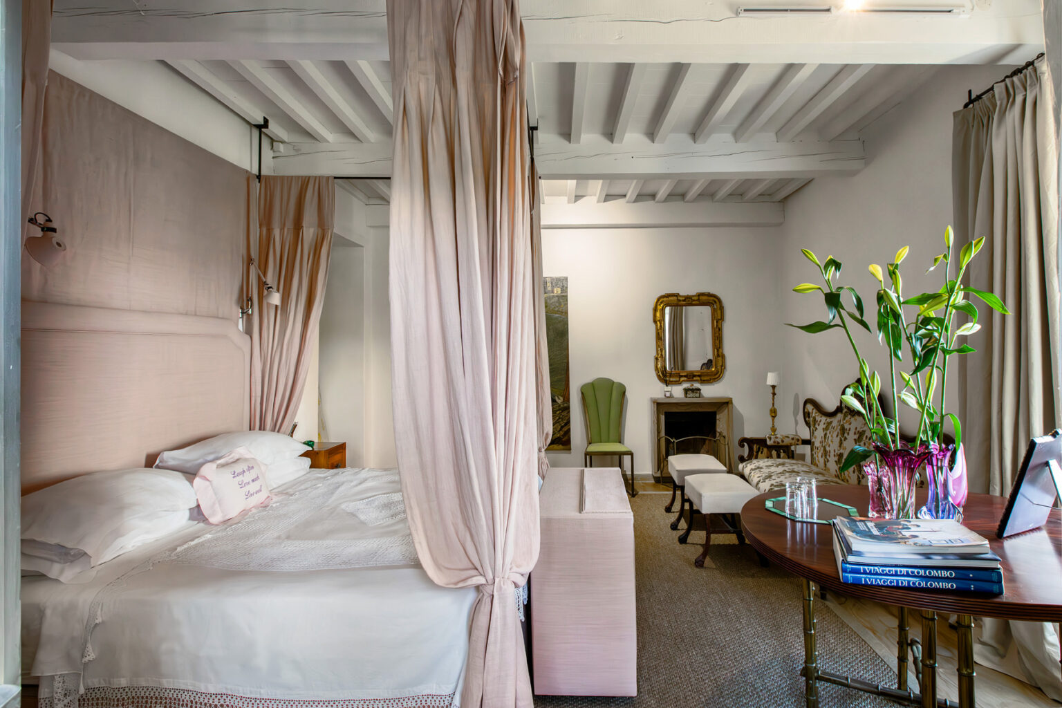 Elegant bedroom interior featuring a four-poster bed with soft drapes, vintage furniture, and a stylish seating area. Fresh flowers in a vase add a touch of nature, while warm lighting and neutral tones create a cozy atmosphere. | Only on SopranoVillas
