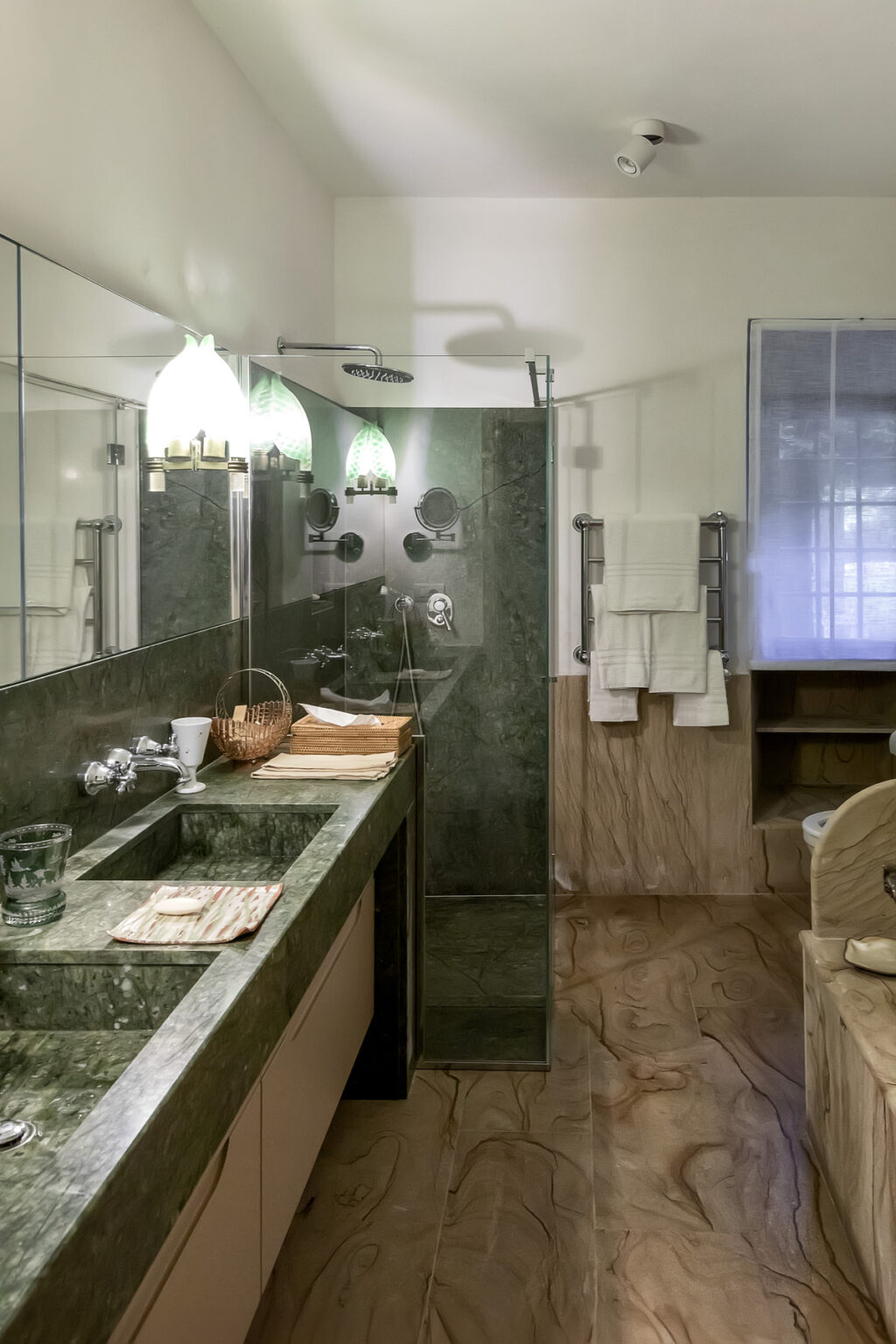Modern bathroom featuring a green marble countertop, a glass shower enclosure, and elegant fixtures. The space includes neatly arranged towels, a woven basket, and soft lighting, creating a serene atmosphere. | Only on SopranoVillas