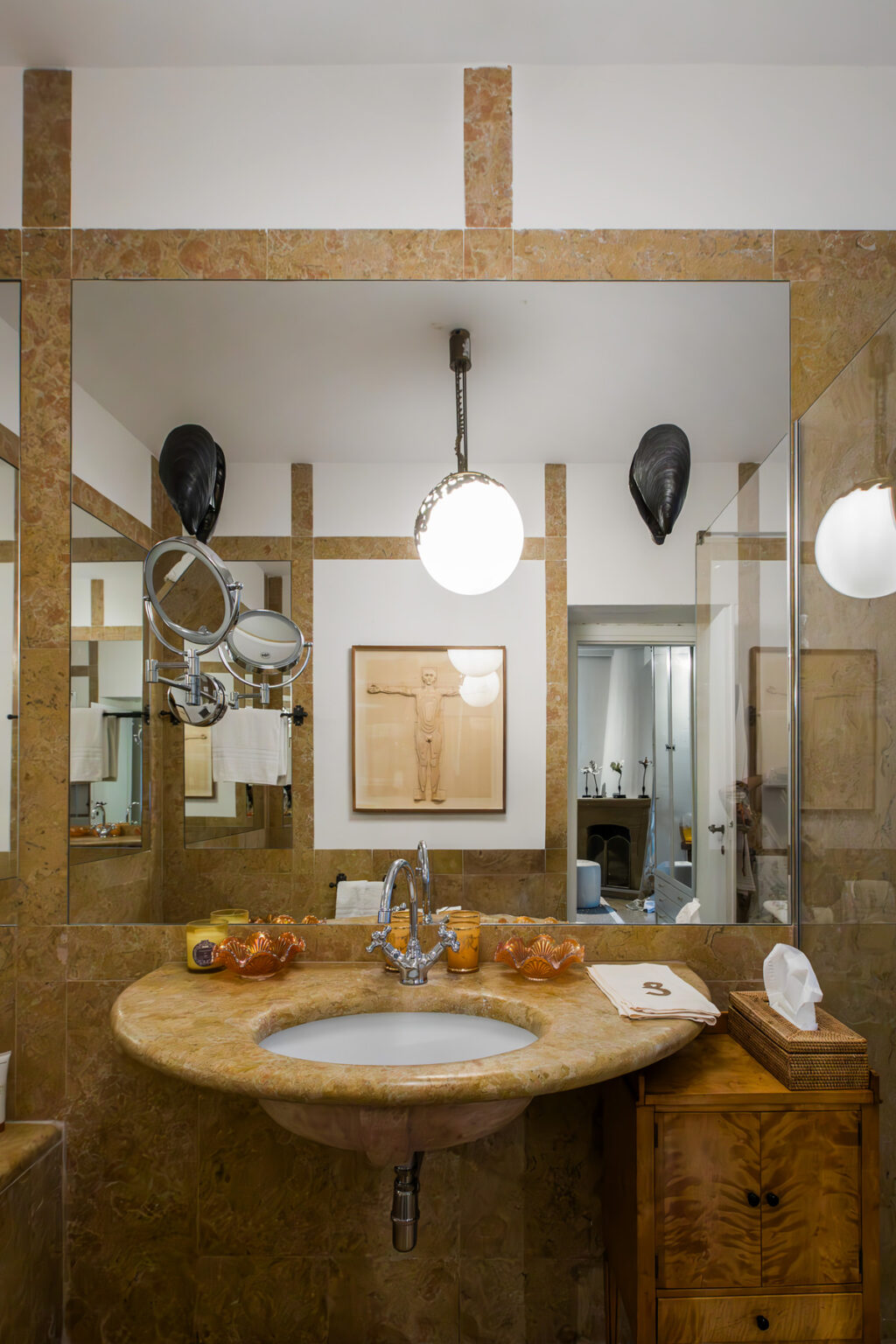 Modern bathroom interior featuring a large mirror, artistic wall decor, unique lighting fixtures, and a stylish sink area with decorative elements. | Only on SopranoVillas