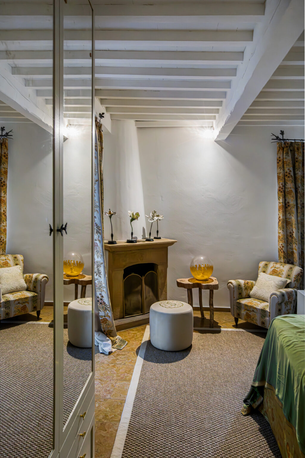 Cozy living room interior featuring two patterned armchairs, a decorative fireplace with a yellow bowl, and a large mirror reflecting the space, accented by floral curtains. | Only on SopranoVillas