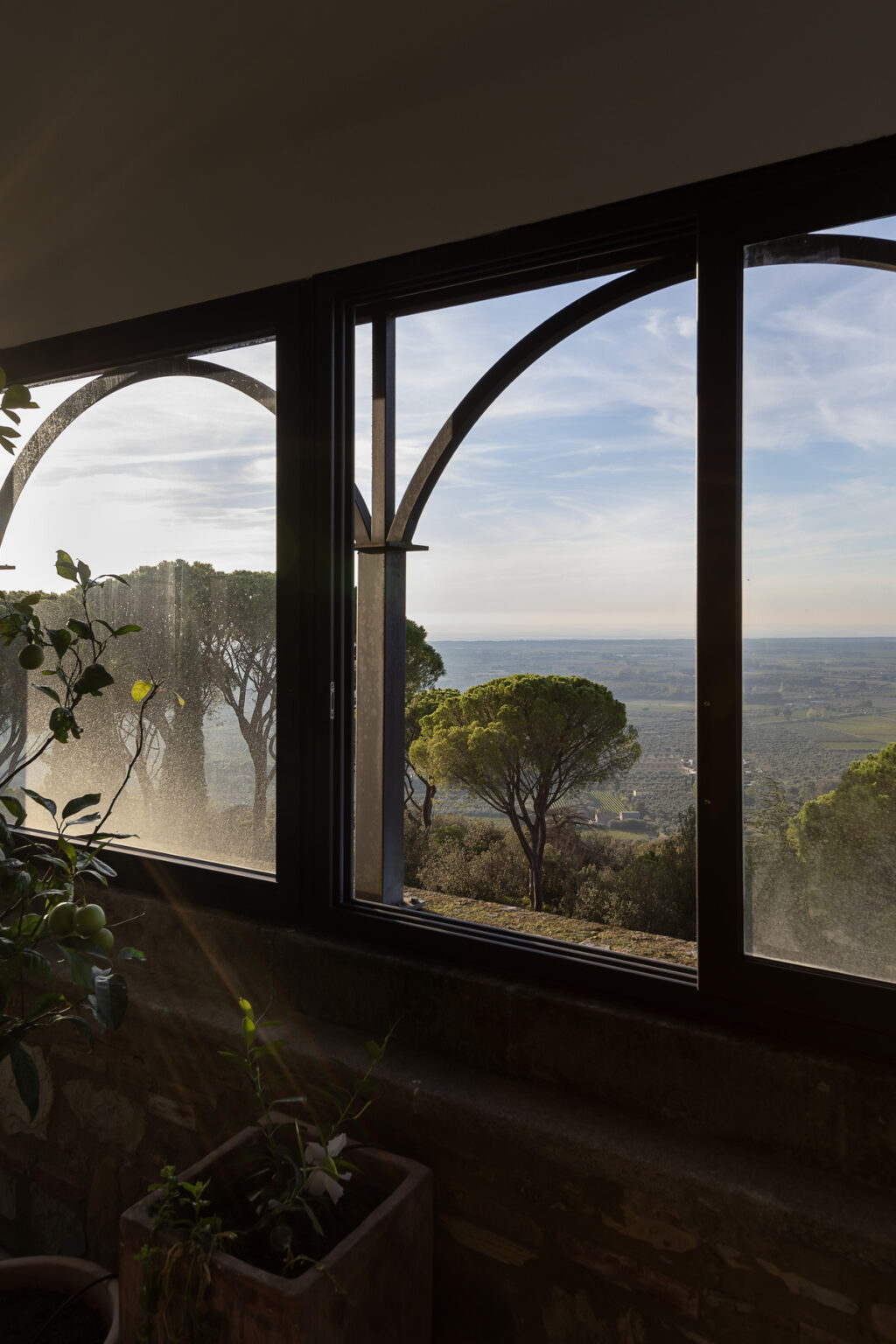 View from a window showcasing a scenic landscape with lush green trees and distant hills under a clear sky. The image captures the tranquility and beauty of nature, emphasizing the connection between indoor and outdoor spaces. | Only on SopranoVillas