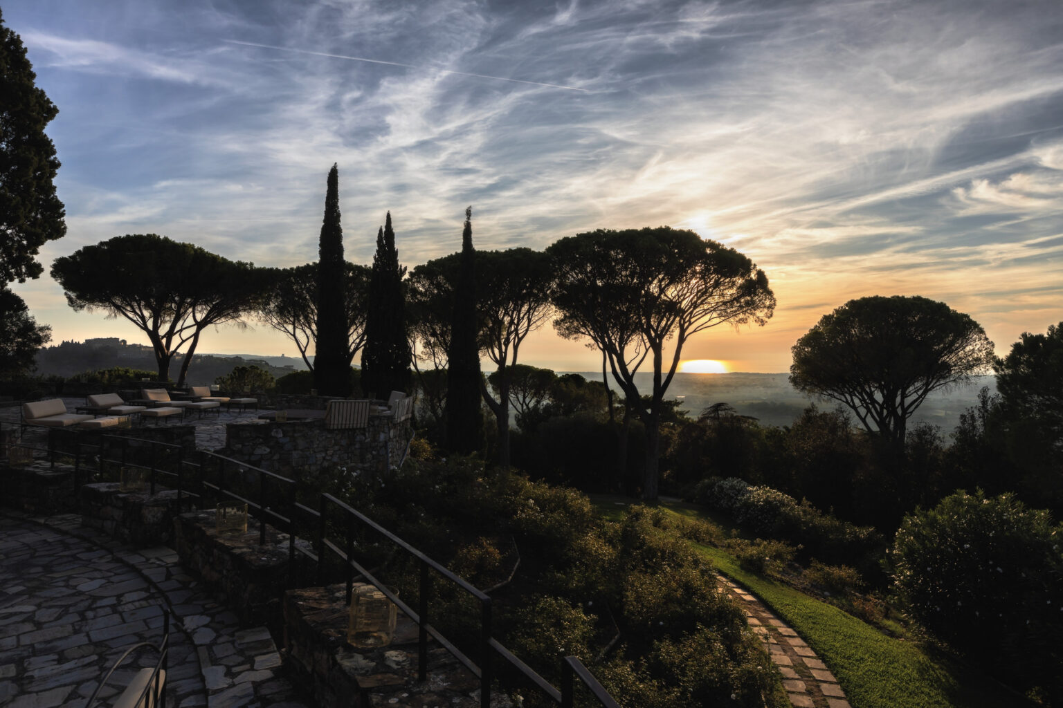 Scenic sunset view over a lush landscape featuring tall trees and a stone pathway, highlighting the beauty of nature and tranquility. | Only on SopranoVillas
