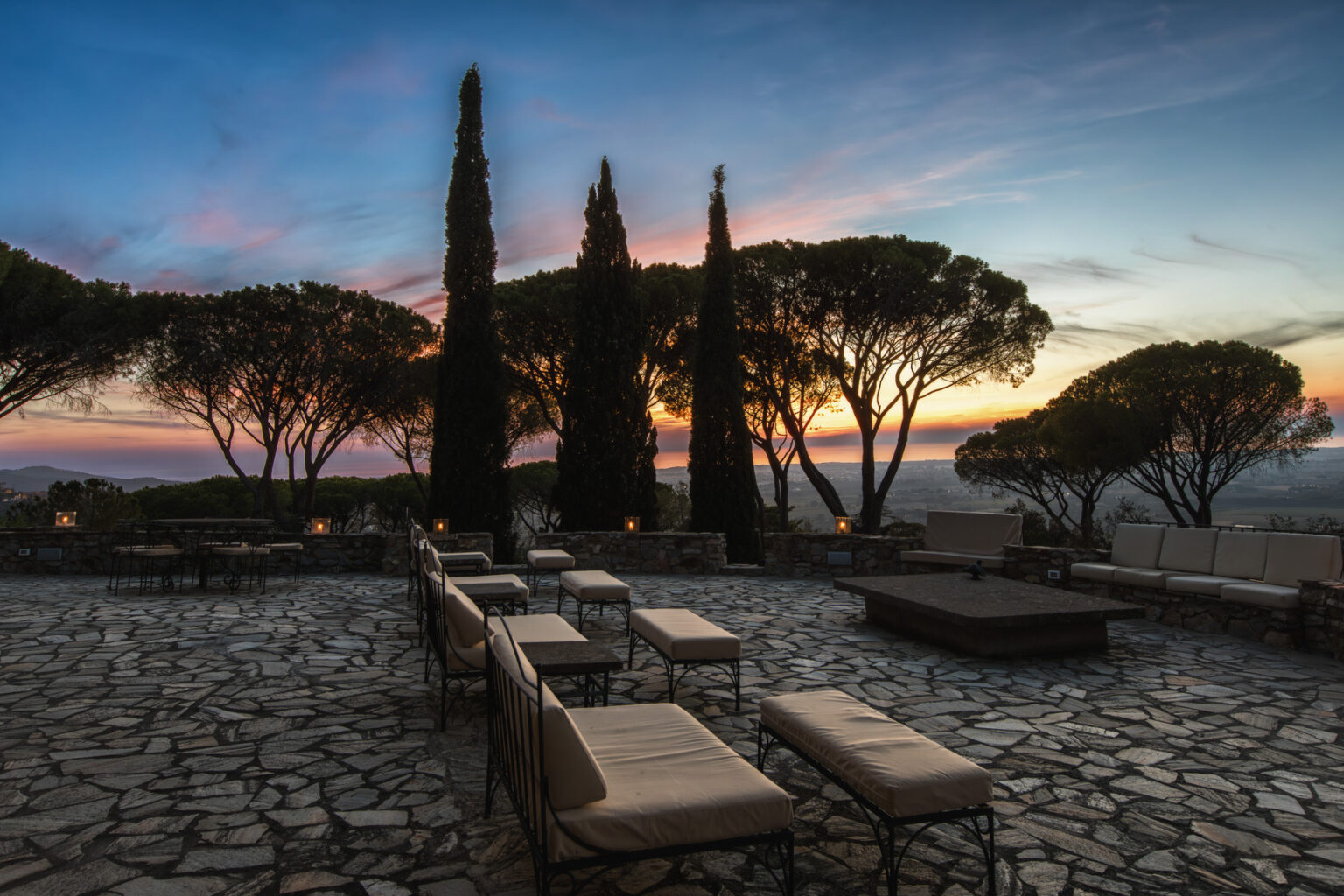 Scenic outdoor patio with lounge chairs and tall trees at sunset, featuring a stone pathway and a tranquil atmosphere. Ideal for relaxation and enjoying nature. | Only on SopranoVillas