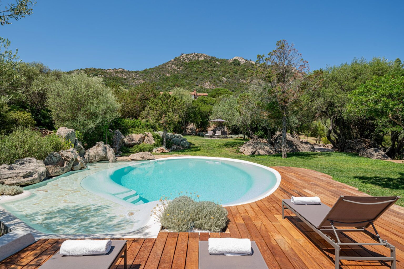 Serene outdoor pool surrounded by lush greenery and wooden decking, perfect for relaxation in a natural setting. | Only on SopranoVillas