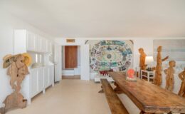 Modern interior design featuring a spacious dining area with a large wooden table, unique wooden sculptures, and a colorful wall mural. Bright, airy space with white cabinetry and natural light. Ideal for showcasing contemporary art and rustic decor elements.