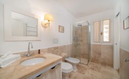 Modern bathroom featuring a glass shower, marble countertops, a stylish sink, and elegant lighting. The design includes neutral tones and a window for natural light.