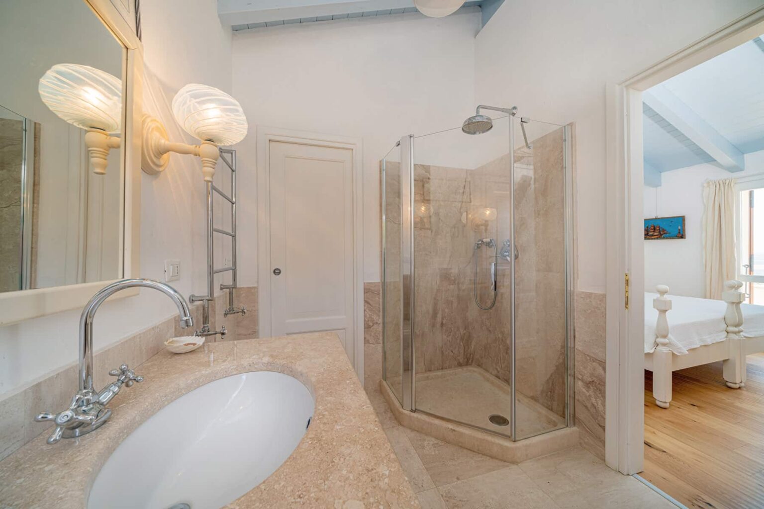 Modern bathroom interior featuring a glass shower enclosure, marble countertop, and elegant lighting fixtures. The design showcases a clean, spacious layout with natural light streaming in from an adjacent room. | Only on SopranoVillas