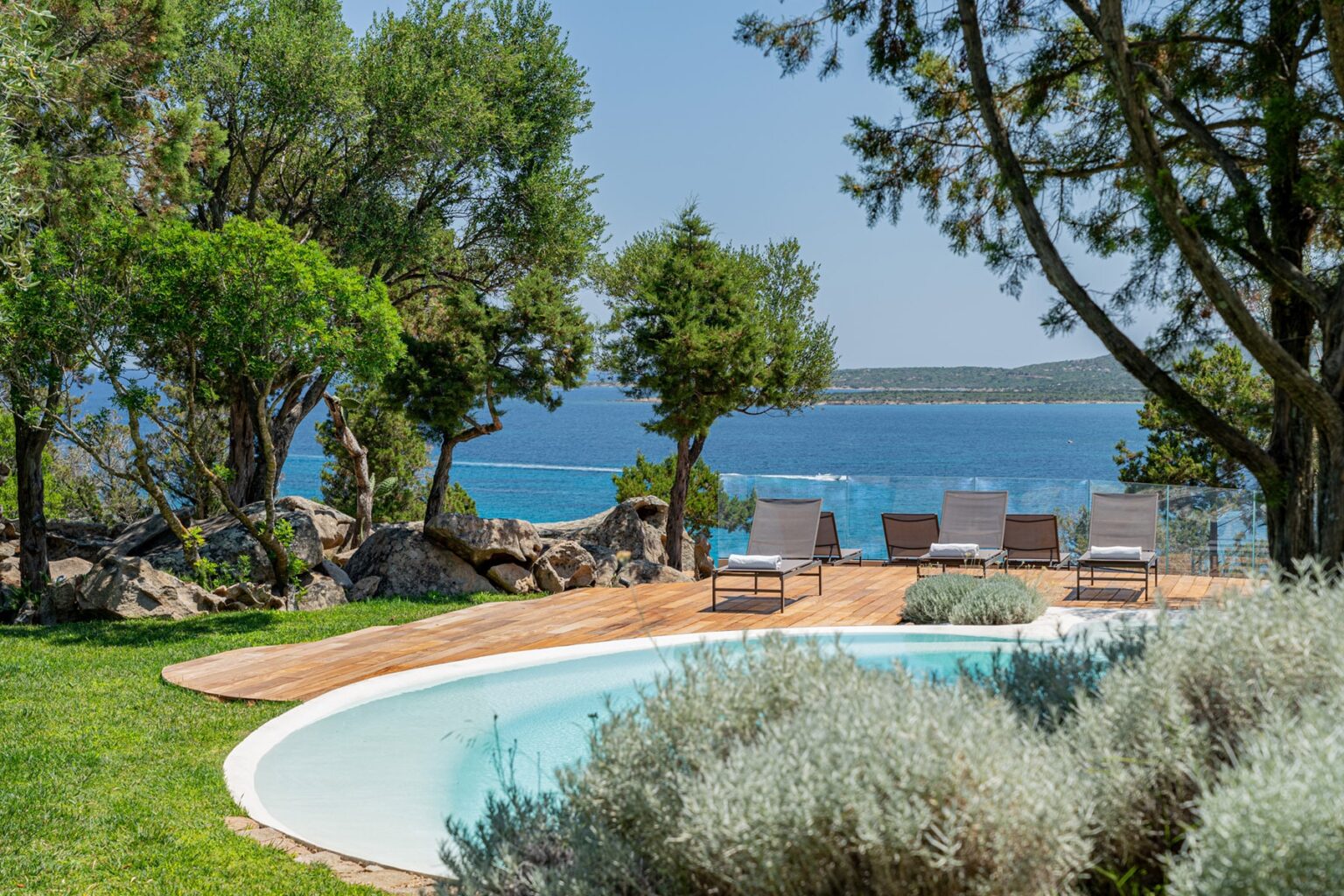 Scenic view of a serene outdoor pool surrounded by lush greenery and lounge chairs, overlooking a tranquil blue sea and distant islands, perfect for relaxation and vacation getaways. | Only on SopranoVillas