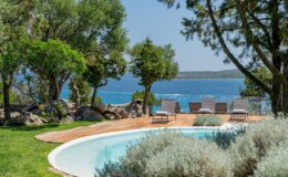 Scenic view of a serene outdoor pool surrounded by lush greenery and lounge chairs, overlooking a tranquil blue sea and distant islands, perfect for relaxation and vacation getaways.