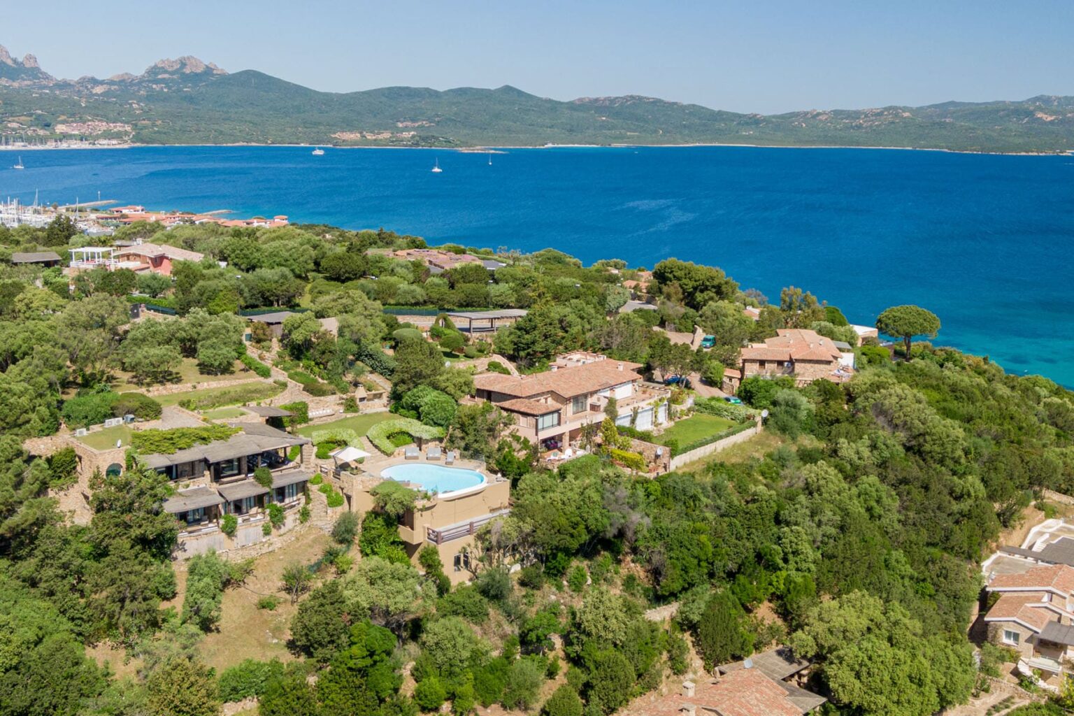 Aerial view of luxurious coastal villas surrounded by lush greenery and blue ocean, showcasing beautiful landscapes and serene environment in a Mediterranean setting. | Only on SopranoVillas