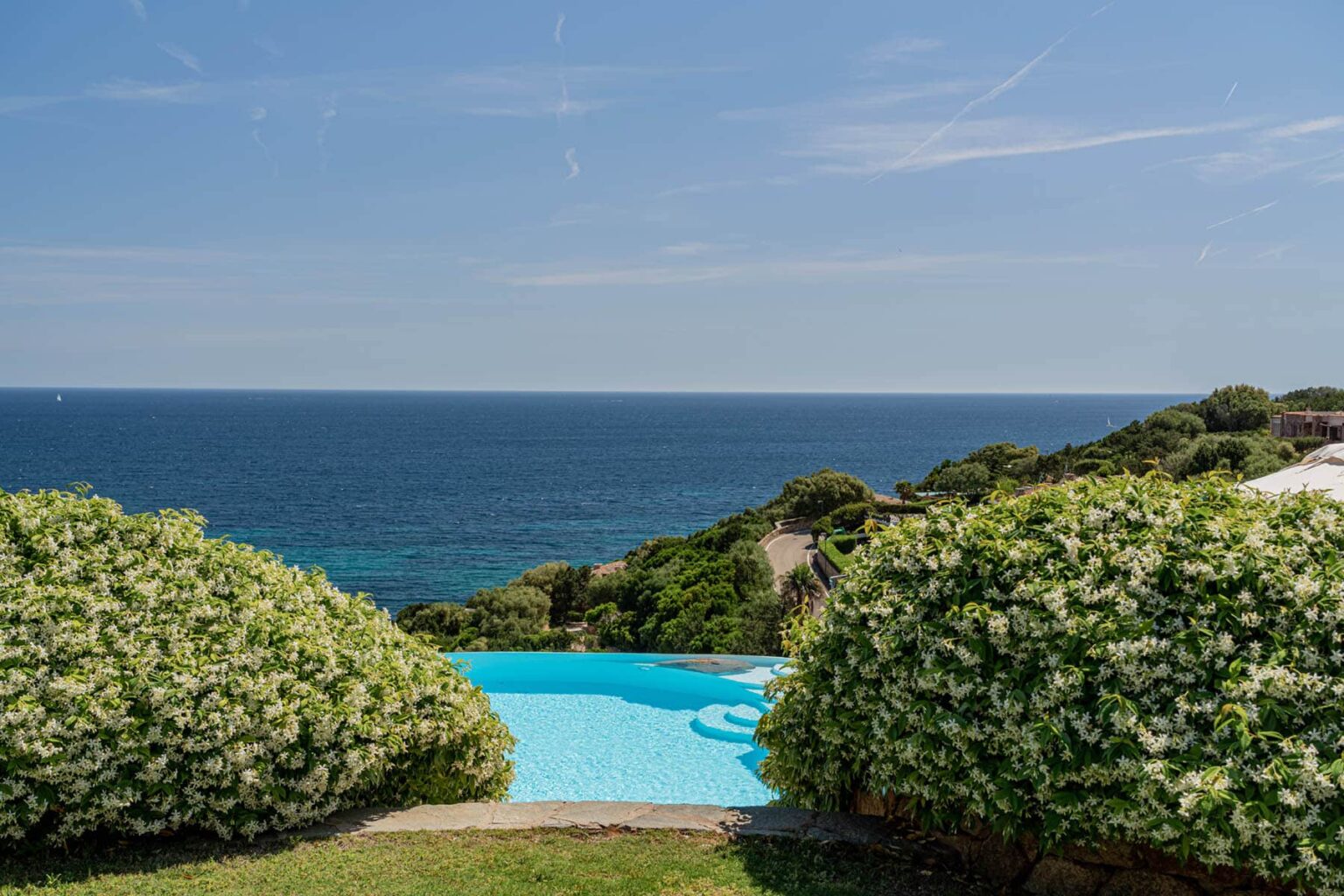 Scenic view of a tranquil infinity pool surrounded by lush greenery, overlooking a serene ocean landscape under a clear blue sky. Perfect for relaxation and vacation inspiration. | Only on SopranoVillas