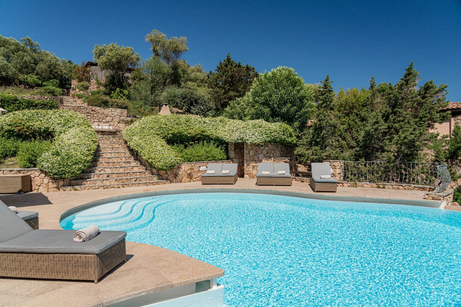 Luxurious outdoor swimming pool surrounded by lush greenery and comfortable lounge chairs, perfect for relaxation in a serene garden setting. | Only on SopranoVillas