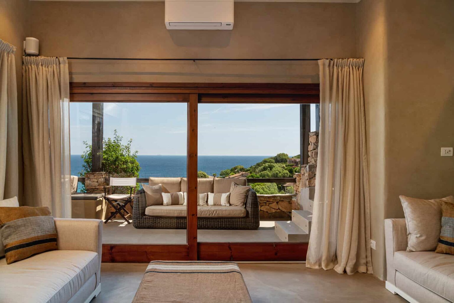 Cozy living room with modern decor, featuring large windows that offer a stunning ocean view. The space includes comfortable seating, neutral tones, and natural light, creating a serene atmosphere. | Only on SopranoVillas