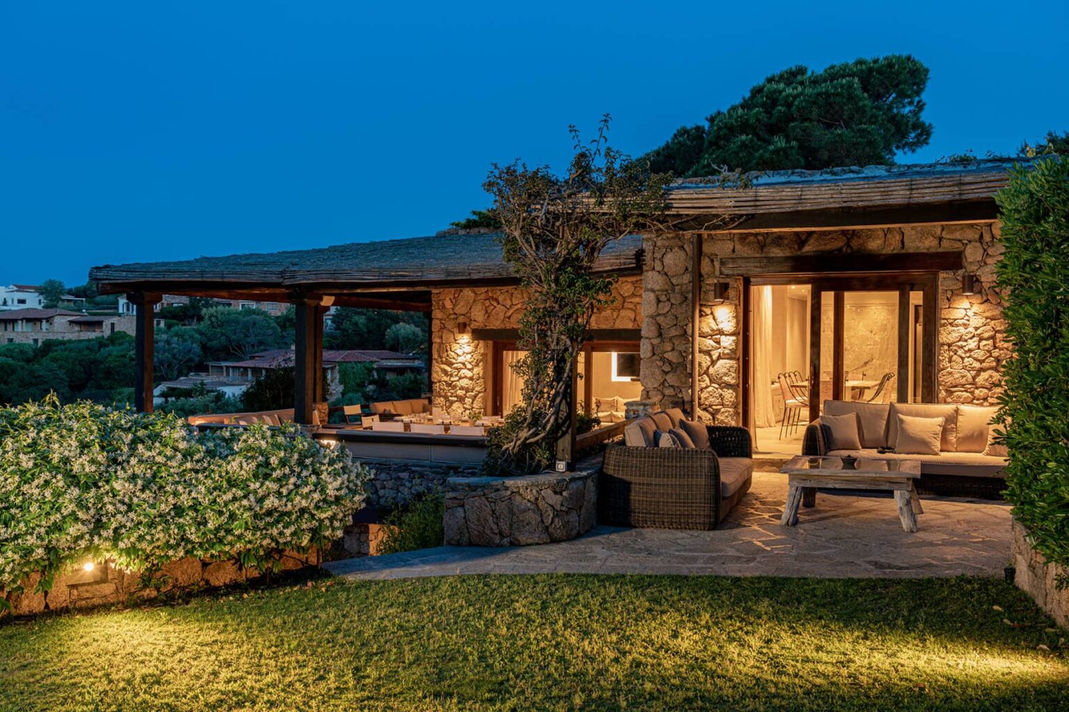 Cozy stone villa exterior at dusk, featuring a spacious terrace with comfortable seating, surrounded by lush greenery and soft outdoor lighting, ideal for relaxation and entertaining. | Only on SopranoVillas