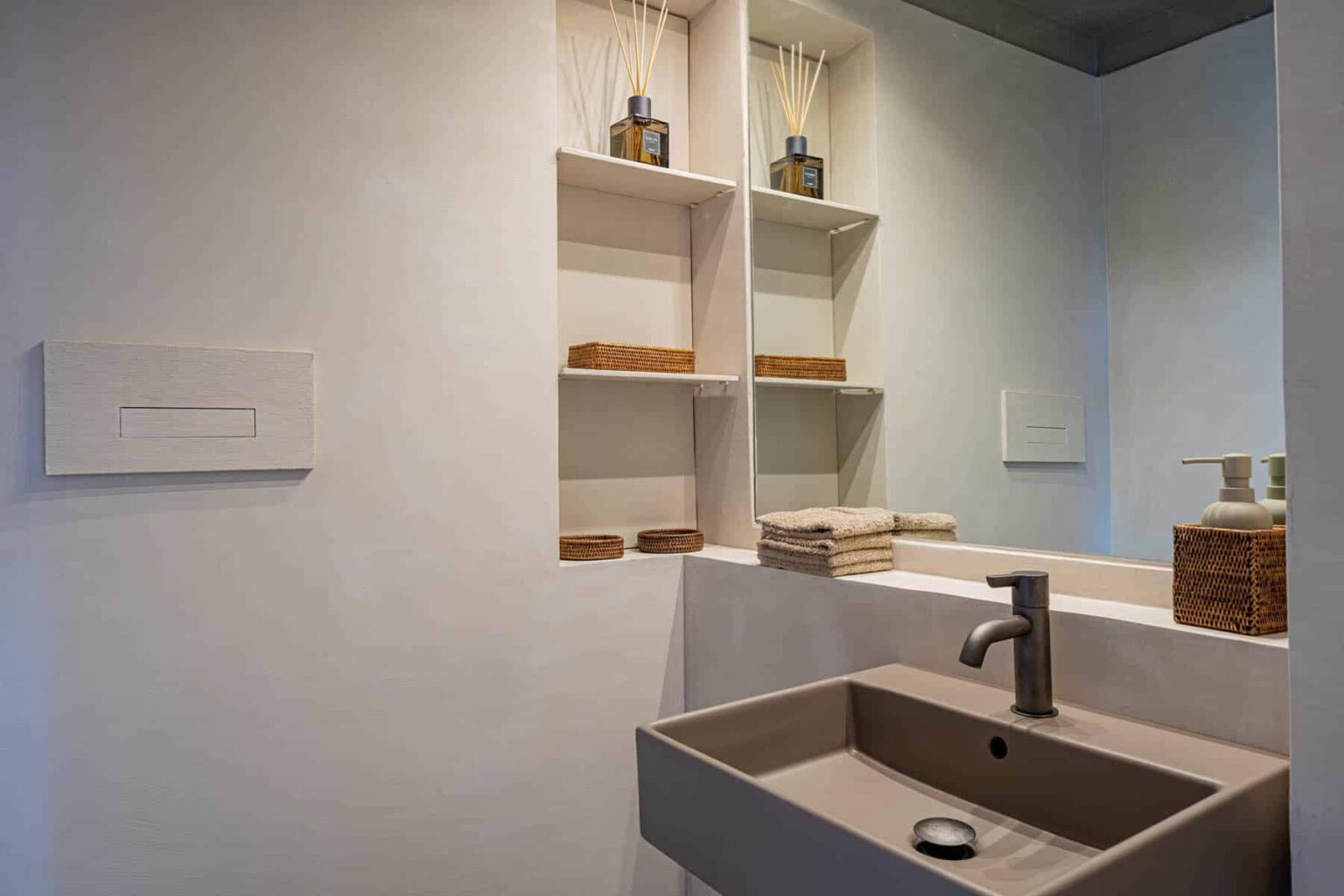 Modern bathroom interior featuring a sleek sink, minimalist shelving with decorative items, and a large mirror, emphasizing a clean and contemporary design. | Only on SopranoVillas