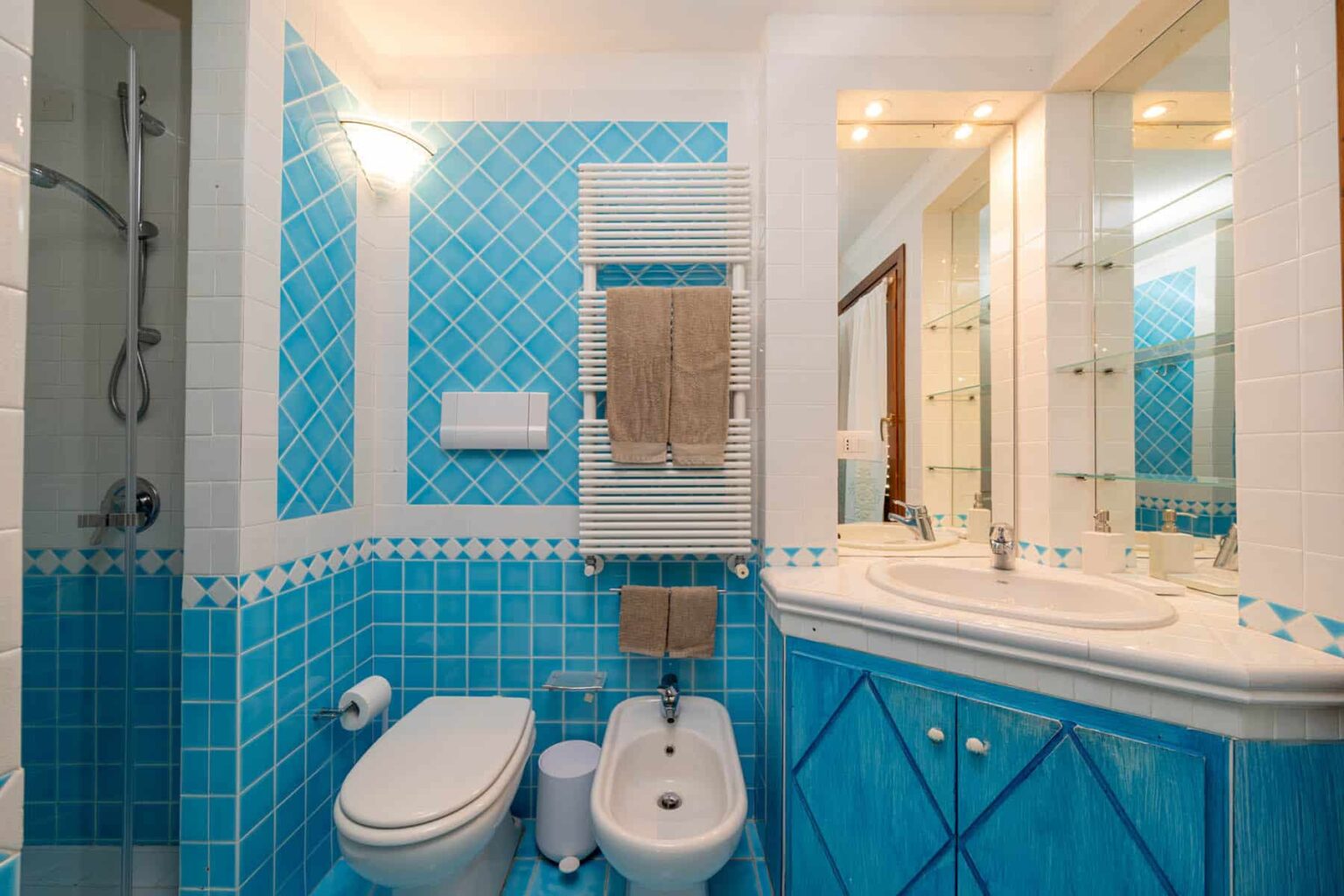 Modern bathroom featuring blue tiled walls, a shower area, a bidet, and a double vanity with mirrors, creating a fresh and vibrant atmosphere. | Only on SopranoVillas
