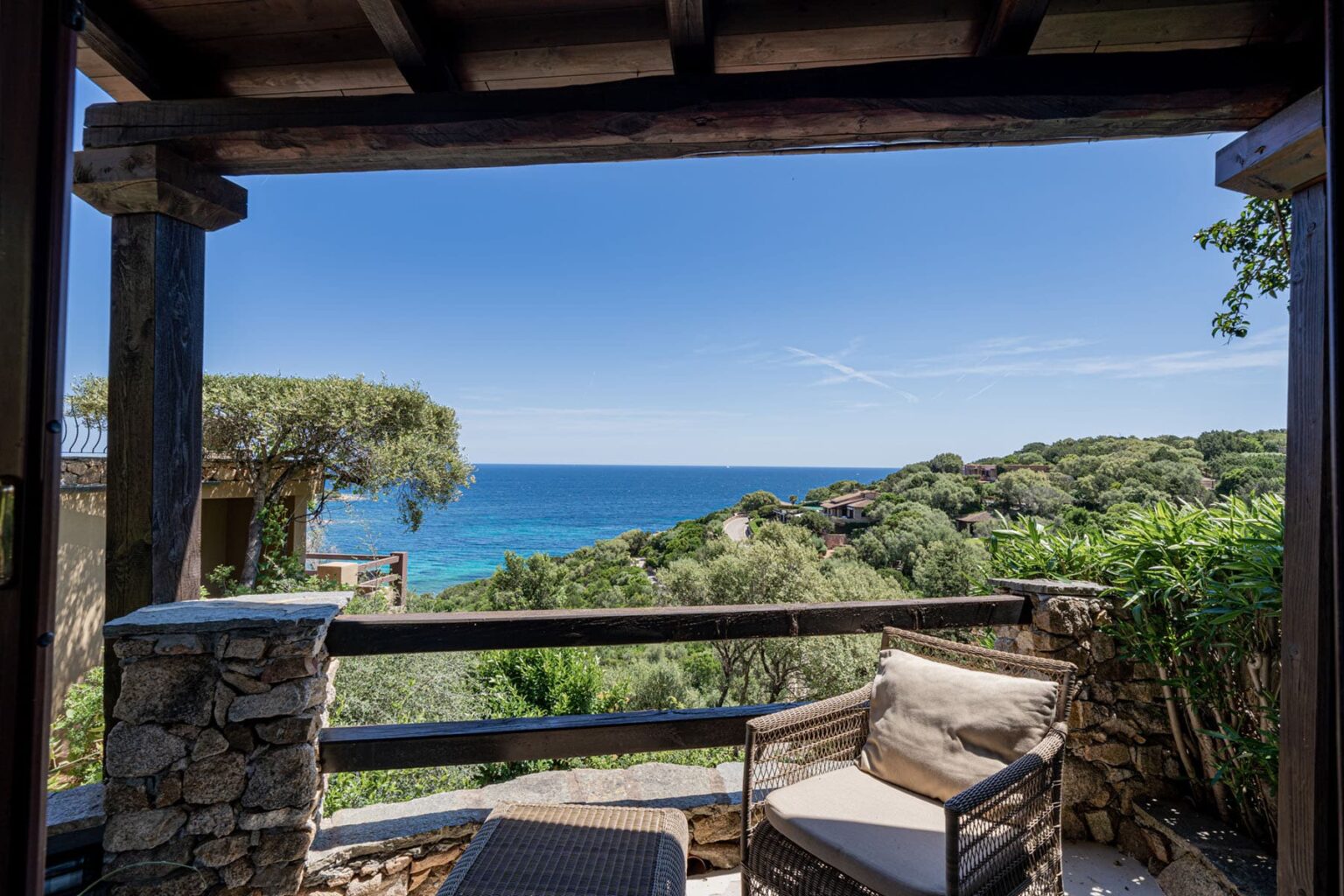 Scenic ocean view from a cozy outdoor seating area, framed by wooden beams and surrounded by lush greenery. Ideal for relaxation and enjoying nature. | Only on SopranoVillas