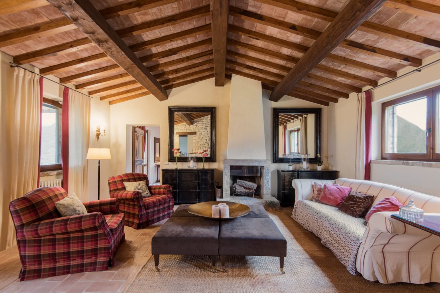 Cozy living room featuring wooden beams, plaid armchairs, a modern sofa, and a stylish coffee table, complemented by large mirrors and natural light from windows. Ideal for relaxation and social gatherings. | Only on SopranoVillas