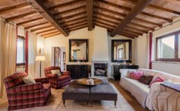 Cozy living room featuring wooden beams, plaid armchairs, a modern sofa, and a stylish coffee table, complemented by large mirrors and natural light from windows. Ideal for relaxation and social gatherings.