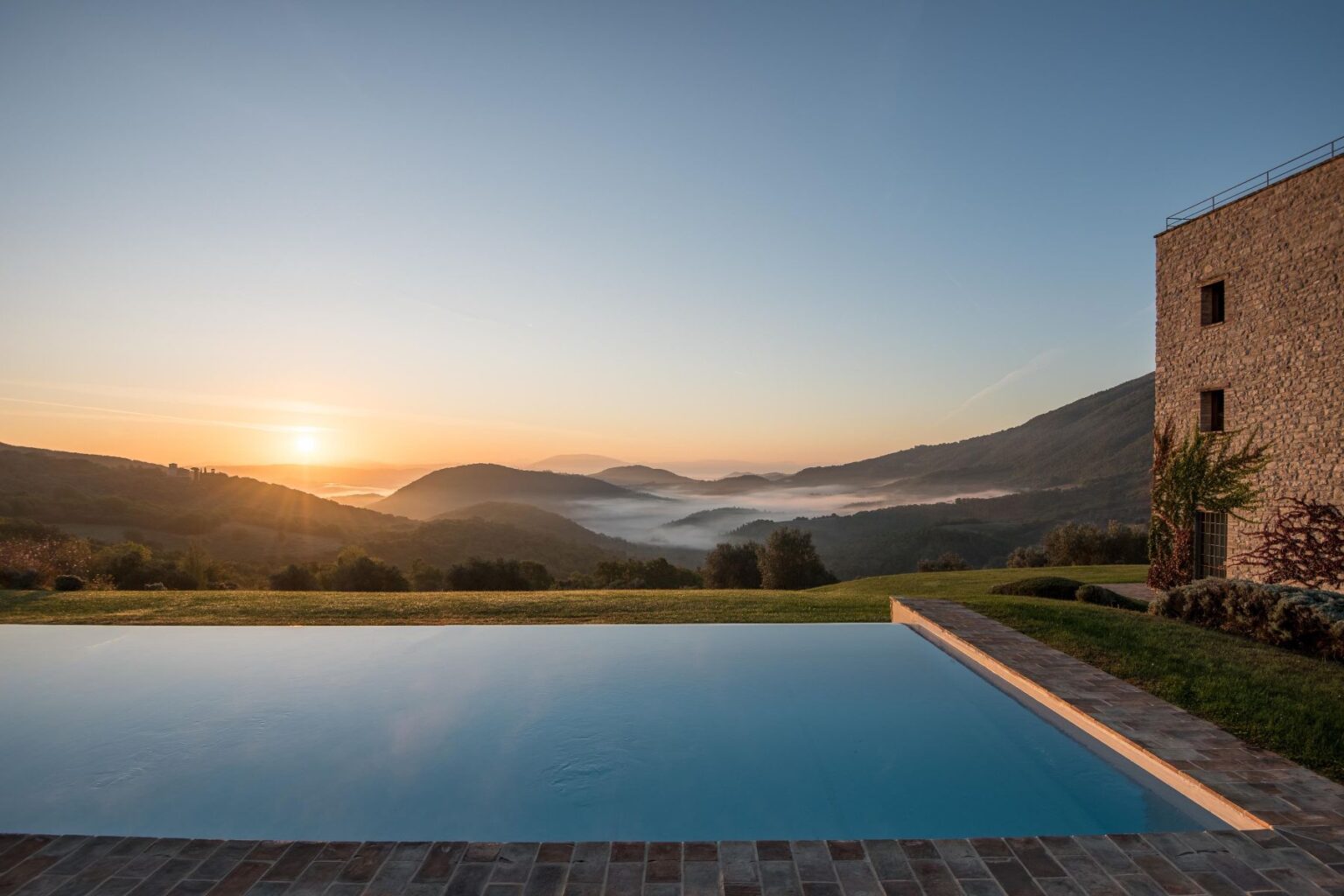 Scenic view of a tranquil infinity pool overlooking misty mountains at sunrise, showcasing lush greenery and a serene landscape. Perfect for vacation rentals or luxury retreats. | Only on SopranoVillas