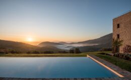 Scenic view of a tranquil infinity pool overlooking misty mountains at sunrise, showcasing lush greenery and a serene landscape. Perfect for vacation rentals or luxury retreats.
