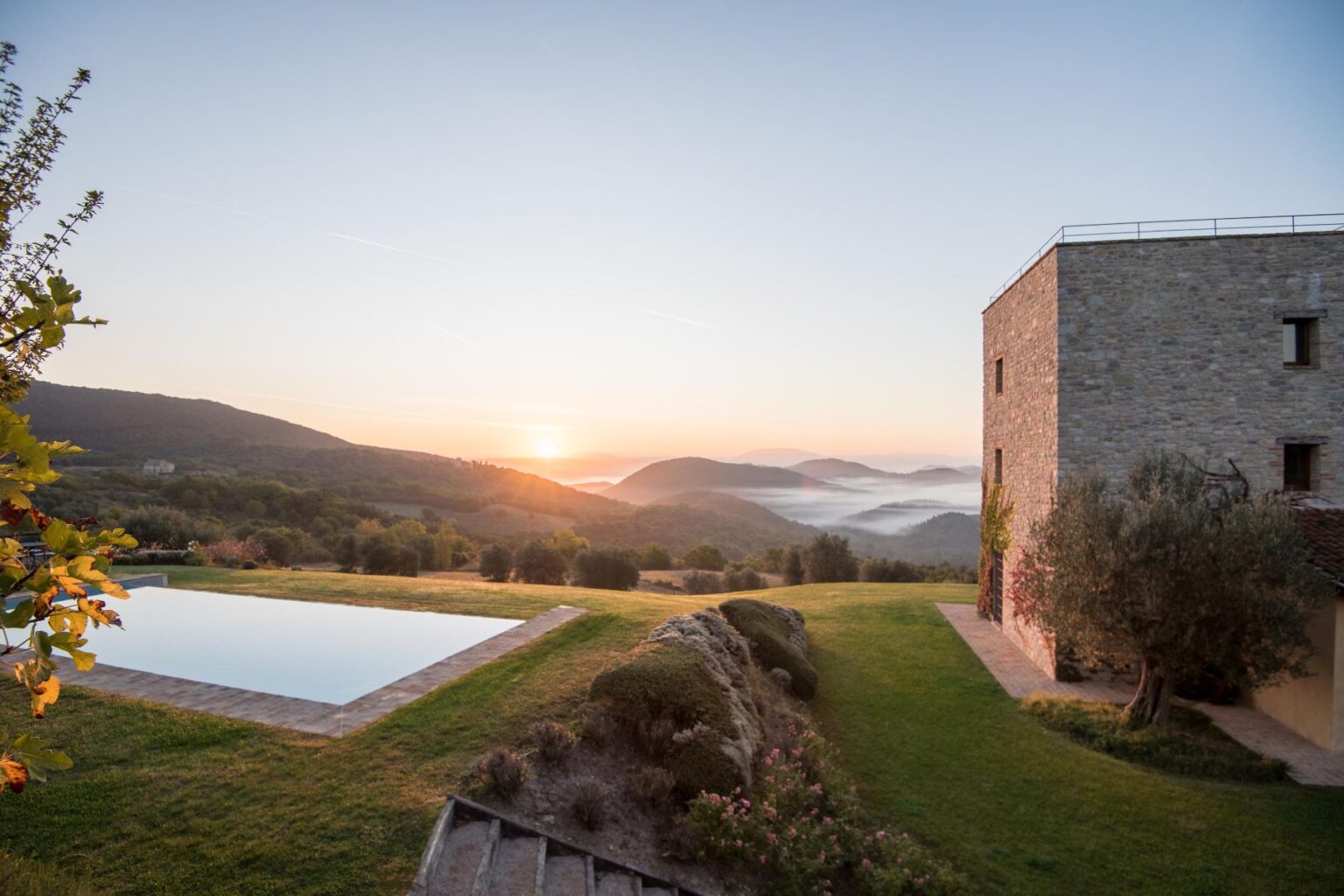 Scenic sunrise view over rolling hills with a stone villa and a tranquil infinity pool, surrounded by lush greenery and misty valleys in the background. | Only on SopranoVillas