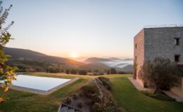 Scenic sunrise view over rolling hills with a stone villa and a tranquil infinity pool, surrounded by lush greenery and misty valleys in the background.