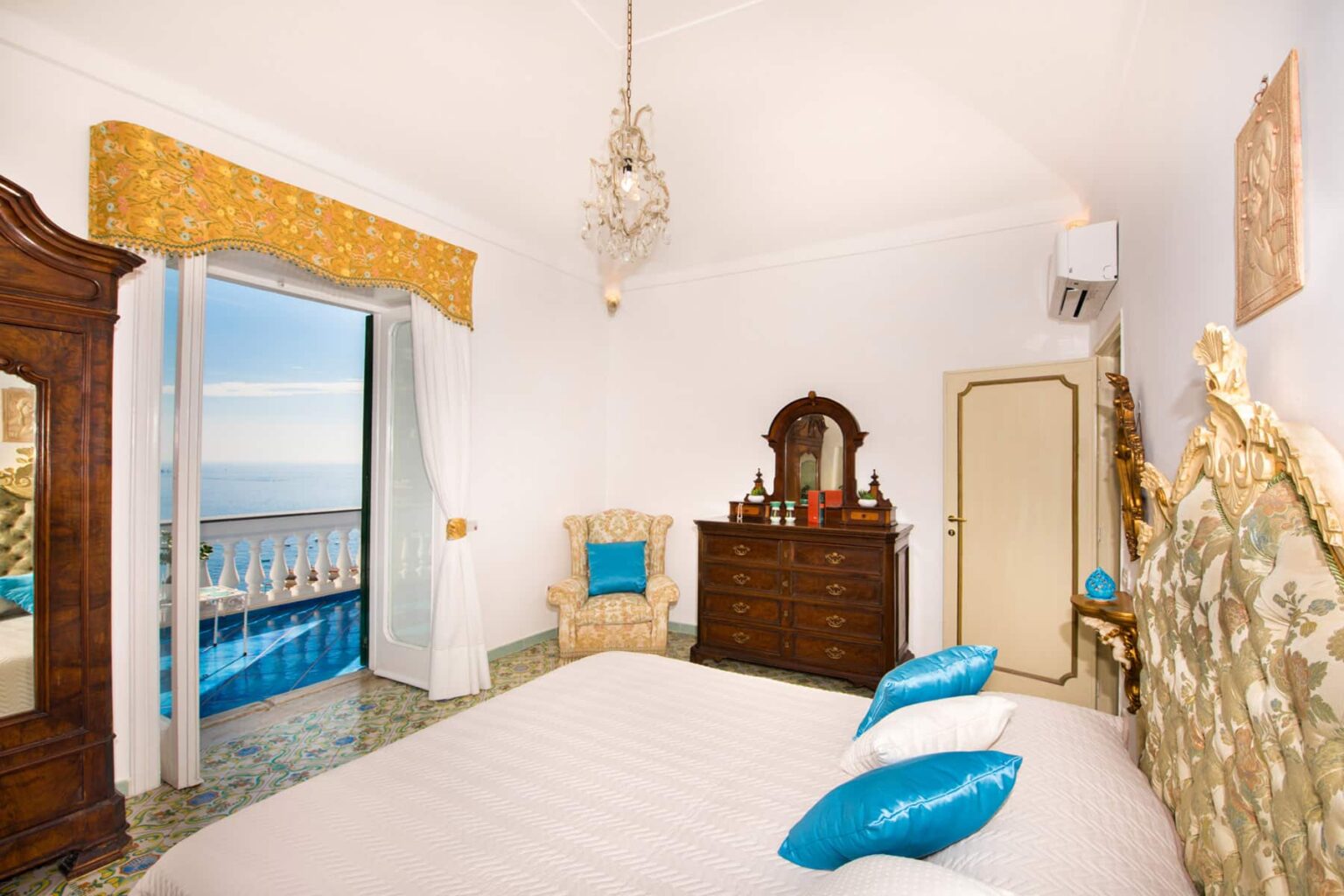 Bright and airy bedroom with ocean views, featuring a comfortable bed with blue pillows, a vintage dresser, and elegant decor, perfect for a relaxing getaway. | Only on SopranoVillas