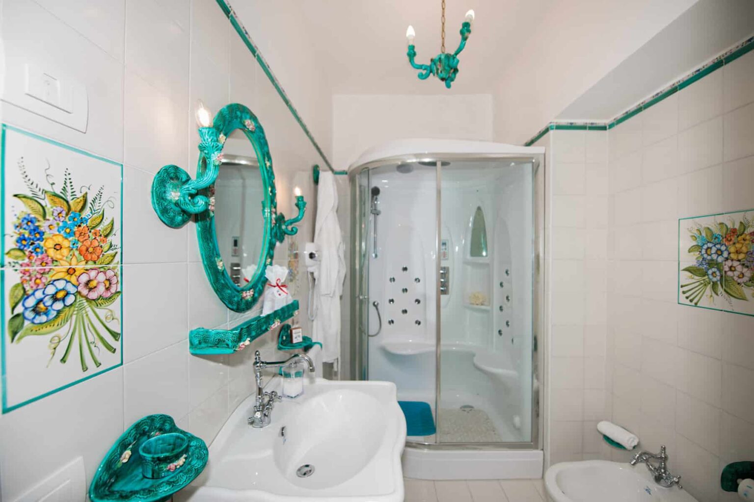 Brightly decorated bathroom featuring turquoise accents, a glass shower enclosure, a stylish sink, and floral artwork on the walls. | Only on SopranoVillas