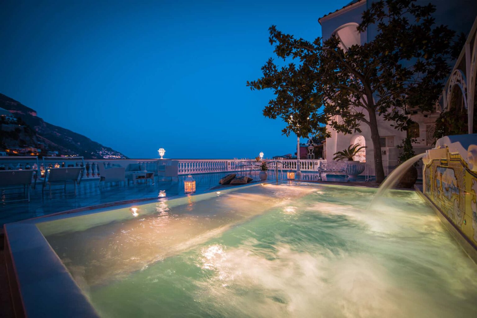 Relaxing outdoor hot tub with a scenic view at dusk, surrounded by lush greenery and soft ambient lighting. Perfect for a romantic getaway or a tranquil evening retreat. | Only on SopranoVillas