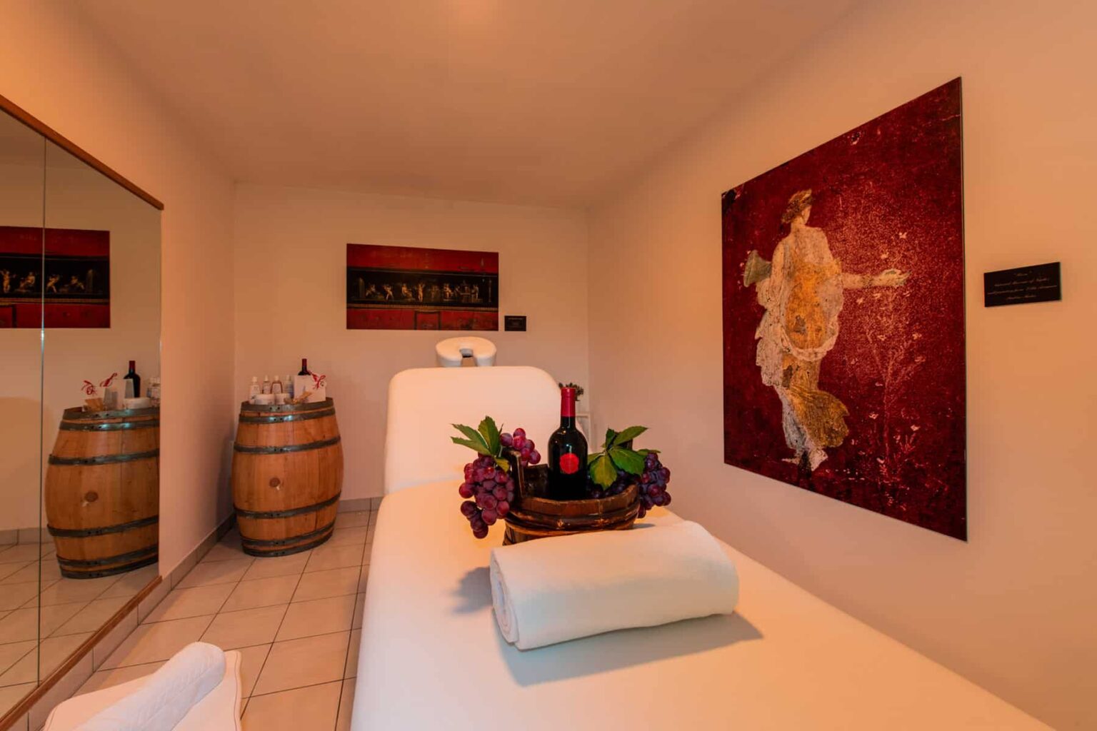 Spa treatment room featuring a massage table adorned with white towels and a decorative fruit basket, surrounded by wooden barrels and vibrant artwork on the walls. Ideal for relaxation and wellness experiences. | Only on SopranoVillas