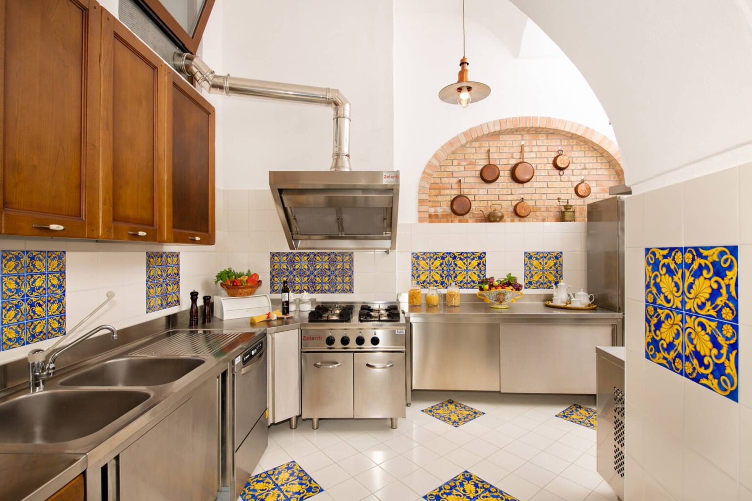 Modern kitchen with stainless steel appliances, wooden cabinets, and colorful tiled accents. Features a spacious layout, professional-grade stove, and decorative wall tiles, creating a bright and inviting cooking space. | Only on SopranoVillas