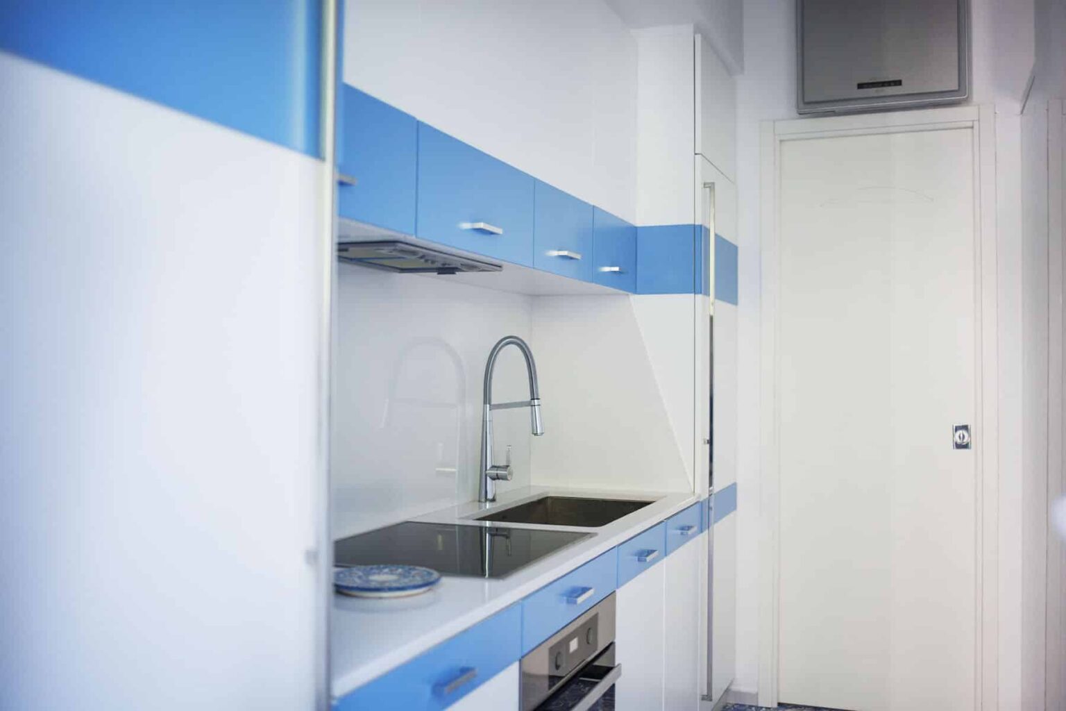 Modern kitchen with blue and white cabinetry, featuring a stainless steel sink and minimalist design elements, ideal for contemporary living spaces. | Only on SopranoVillas