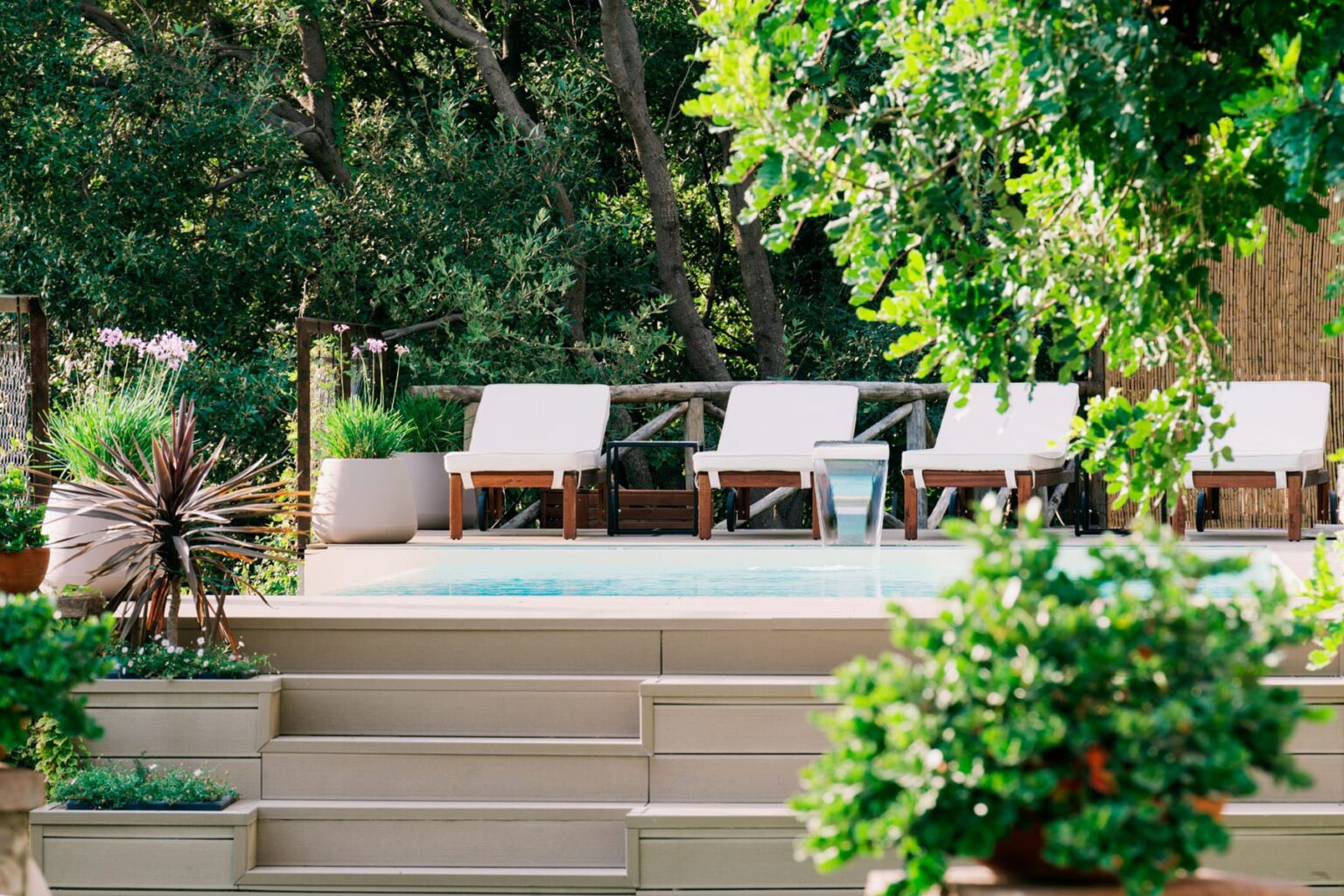 Serene outdoor pool area featuring comfortable lounge chairs surrounded by lush greenery and potted plants, ideal for relaxation and leisure. | Only on SopranoVillas