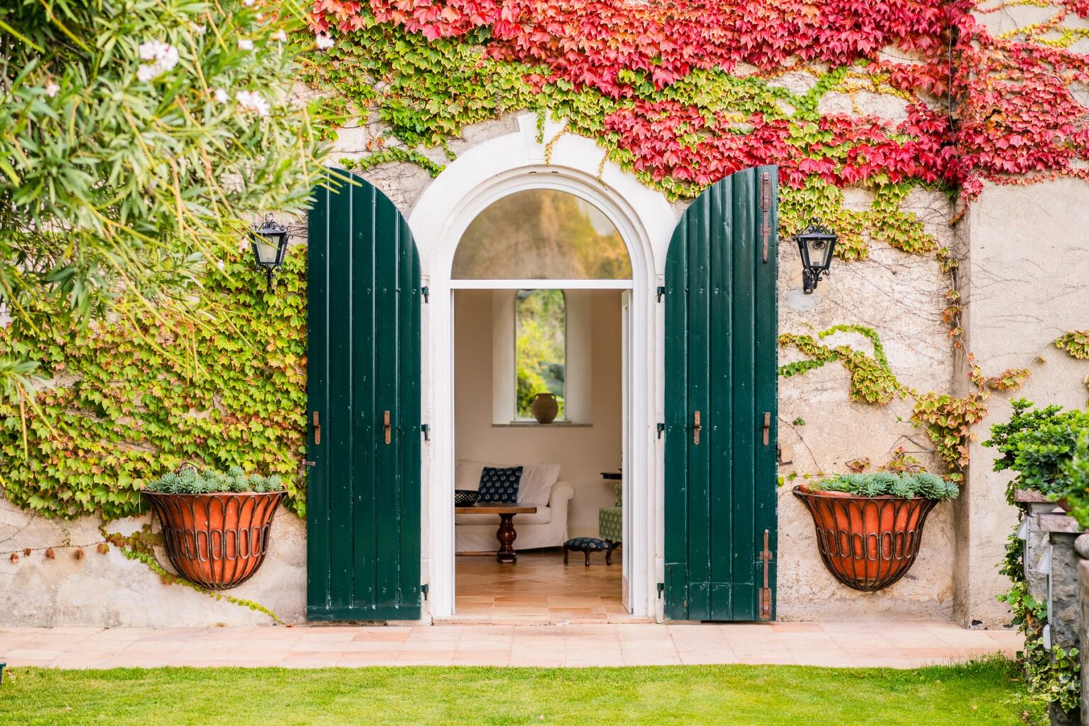 Charming entrance with green wooden doors framed by vibrant ivy and potted plants, leading into a bright and inviting interior space. | Only on SopranoVillas