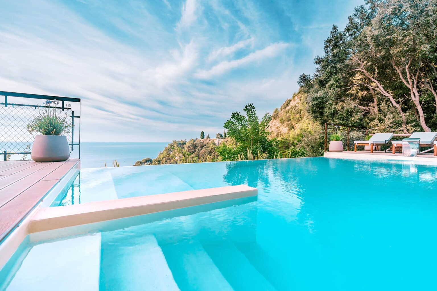 Modern infinity pool overlooking a serene ocean view, surrounded by lush greenery and a clear blue sky. Ideal for luxury vacation rentals or resort marketing. | Only on SopranoVillas