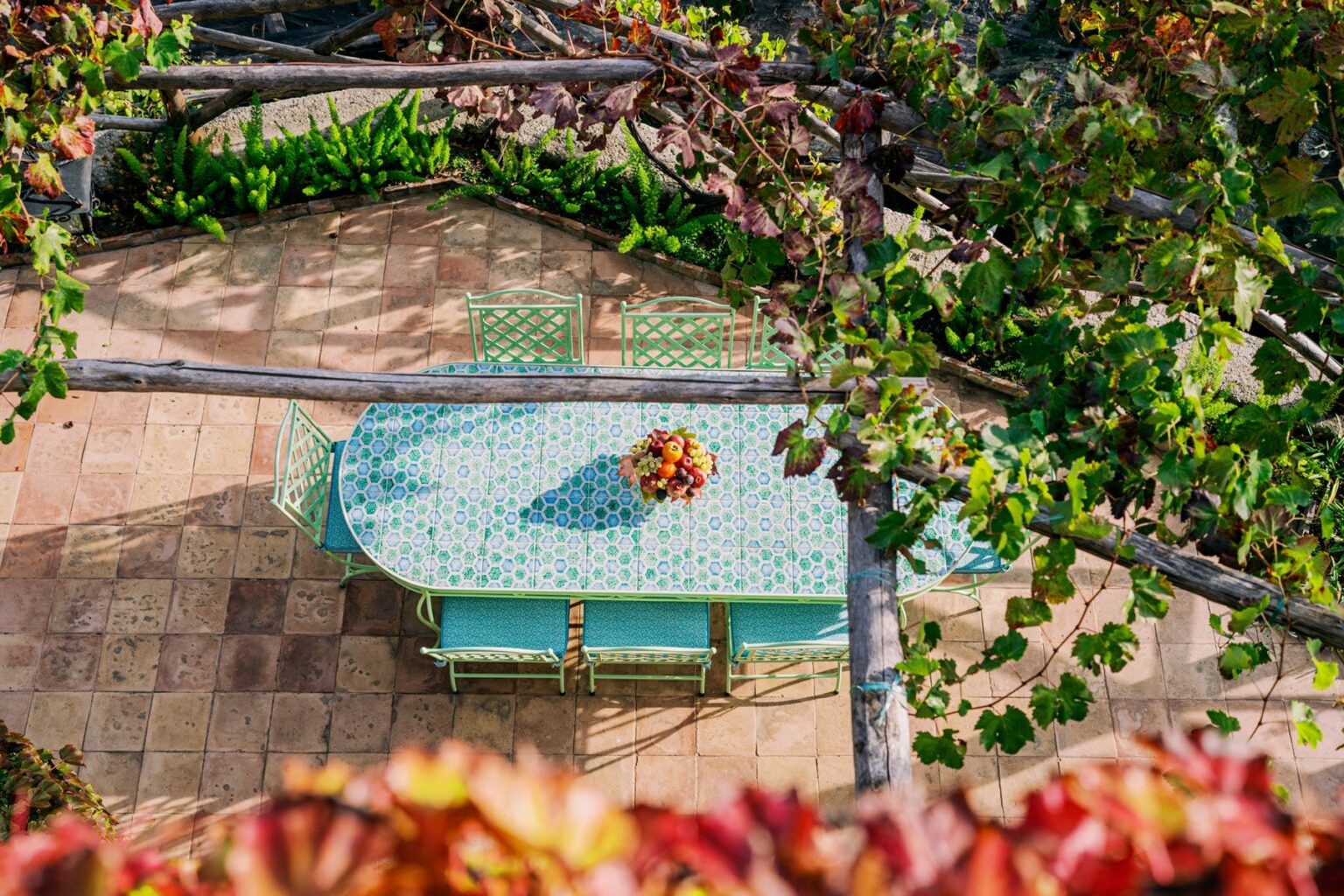 Aerial view of a turquoise outdoor dining table adorned with a floral centerpiece, surrounded by lush greenery and autumn leaves on a stone patio. | Only on SopranoVillas