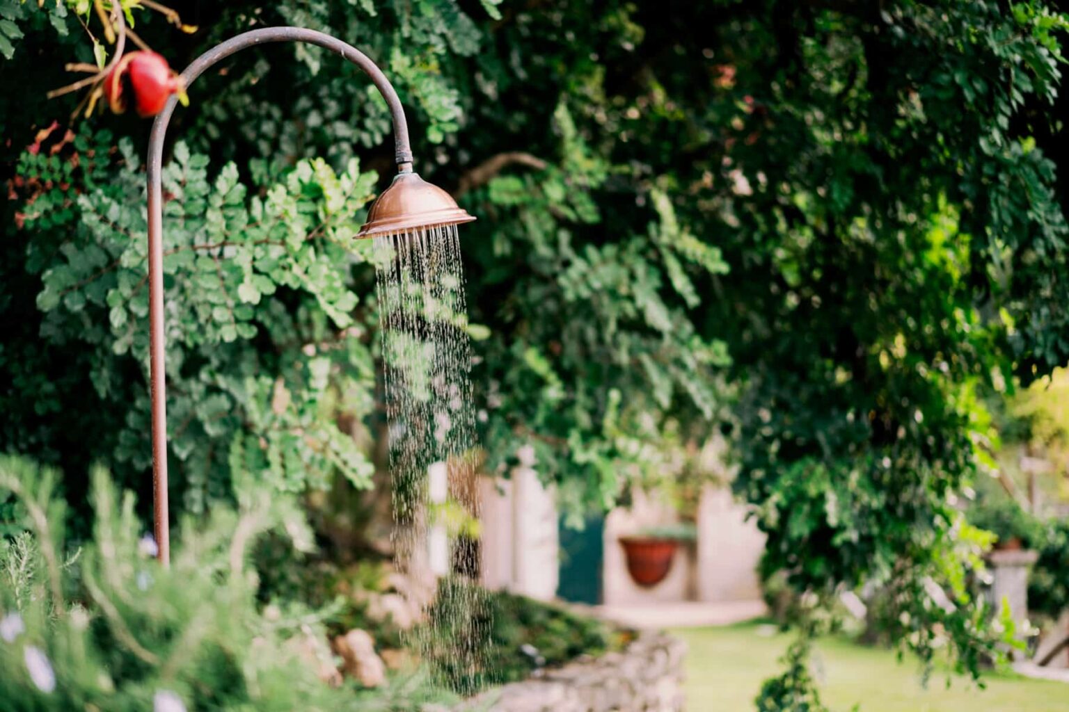 Outdoor copper shower surrounded by lush greenery in a garden setting, with water cascading down from the showerhead. | Only on SopranoVillas