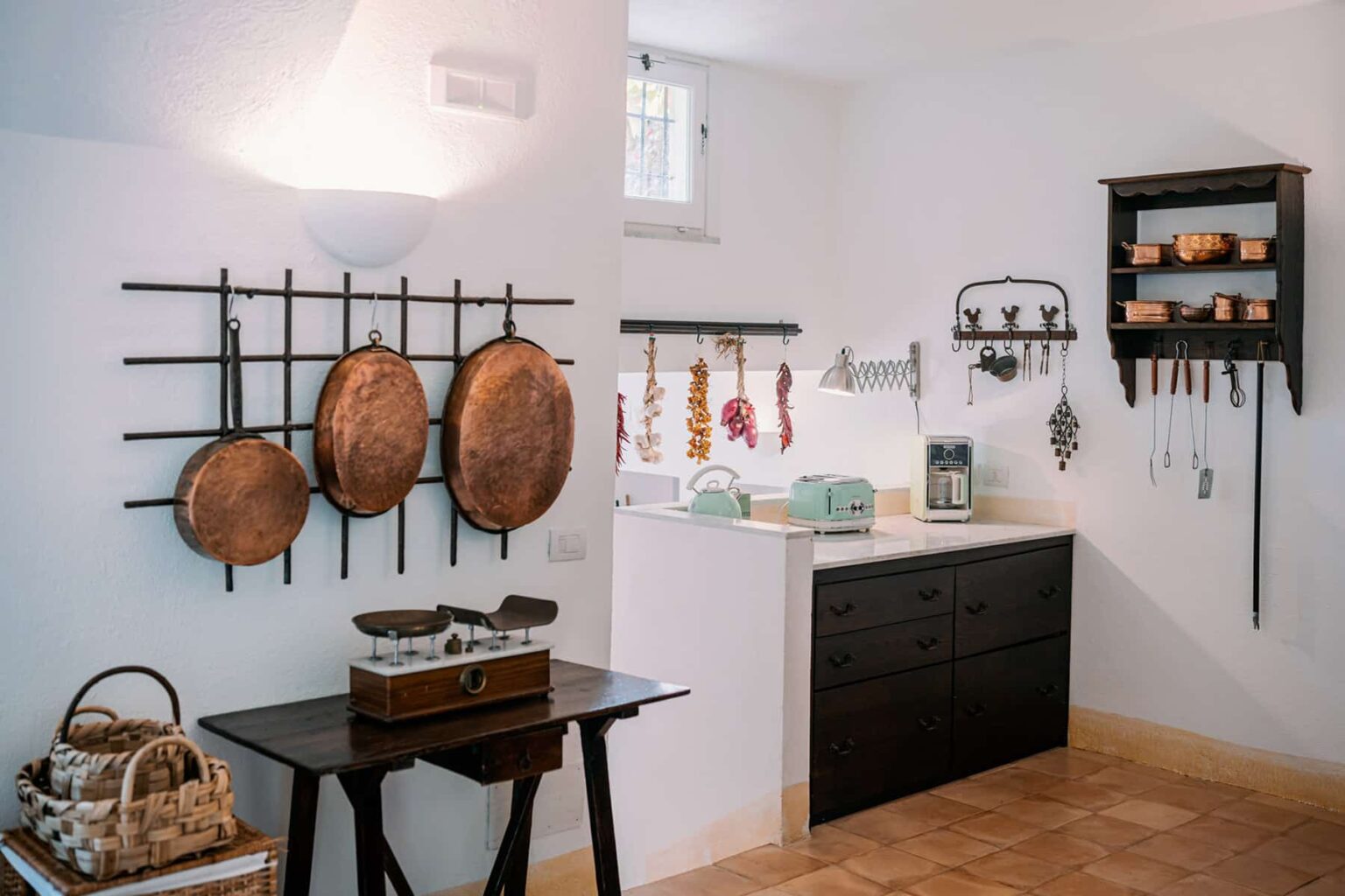 Modern kitchen interior featuring black cabinetry, wooden cookware displayed on wall racks, and a cozy dining table with baskets, creating a stylish and functional cooking space. | Only on SopranoVillas