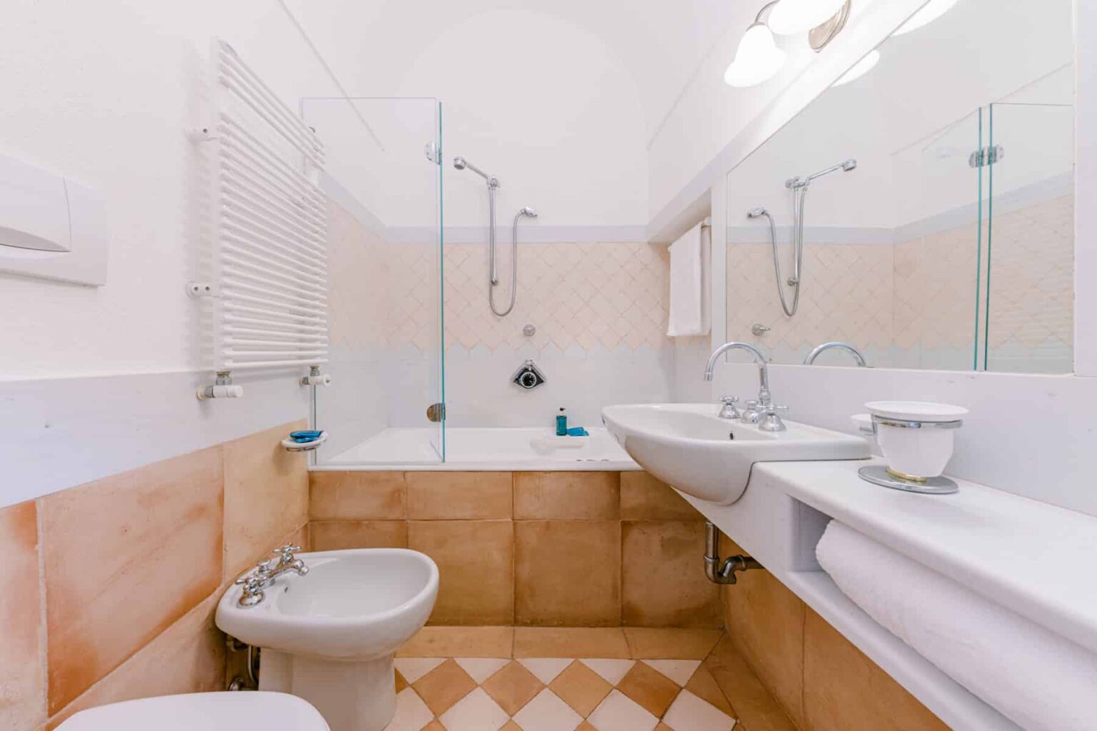 Modern bathroom featuring a glass shower, bathtub, double sink, and bidet, with beige tiles and ample natural light. Ideal for showcasing contemporary interior design. | Only on SopranoVillas