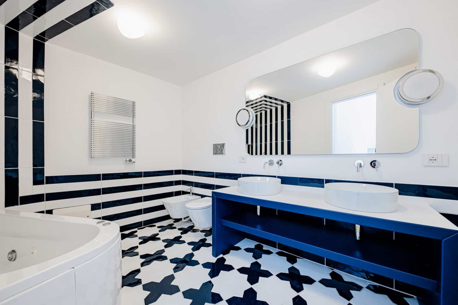 Modern bathroom design featuring a blue and white color scheme, a large mirror, dual sinks, and a stylish bathtub. The floor showcases intricate tile patterns, enhancing the contemporary aesthetic. | Only on SopranoVillas