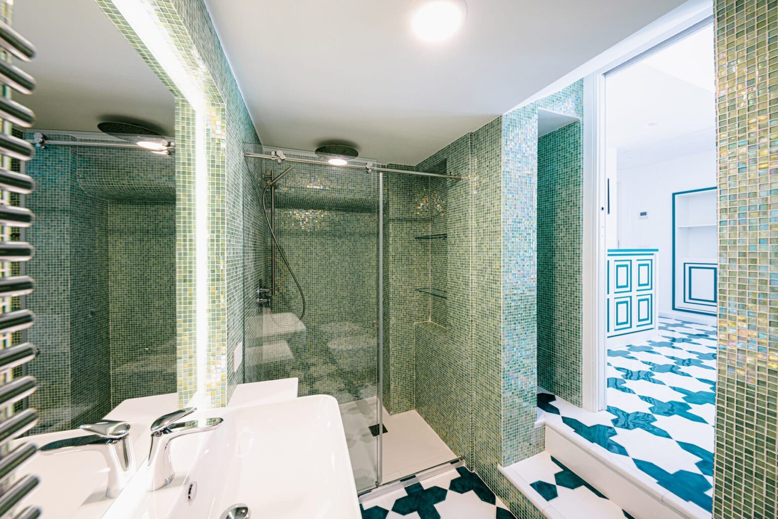 Modern bathroom interior featuring green mosaic tiles, a glass shower enclosure, and a stylish sink. The design includes a vibrant patterned floor and contemporary fixtures, creating a fresh and inviting atmosphere. | Only on SopranoVillas