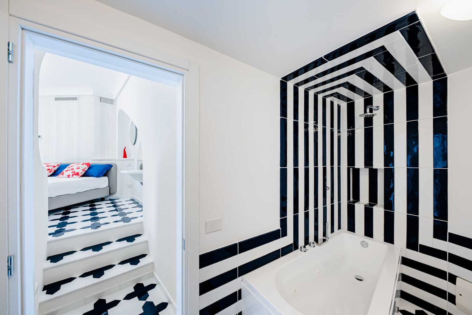 Modern bathroom featuring a striking black and white striped tile design, showcasing a sleek bathtub and an open doorway leading to a stylish living area with patterned flooring. | Only on SopranoVillas