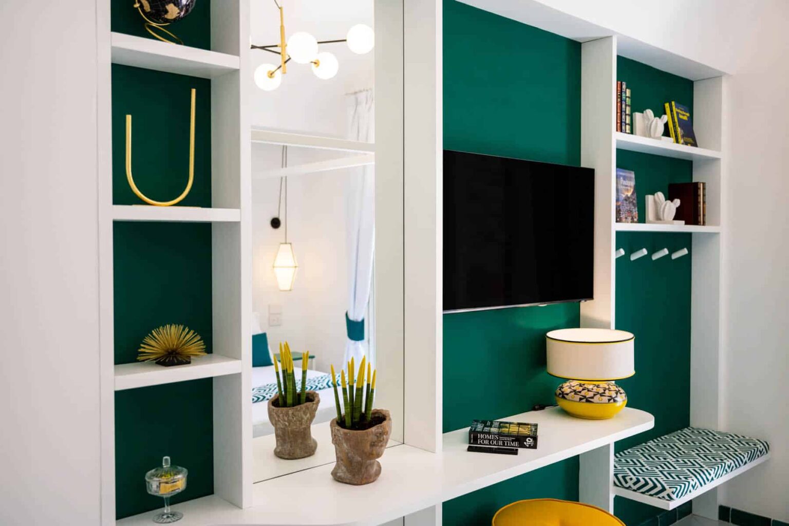 Modern living room interior featuring a green accent wall, white shelving units, a flat-screen TV, decorative plants, and stylish lighting. | Only on SopranoVillas